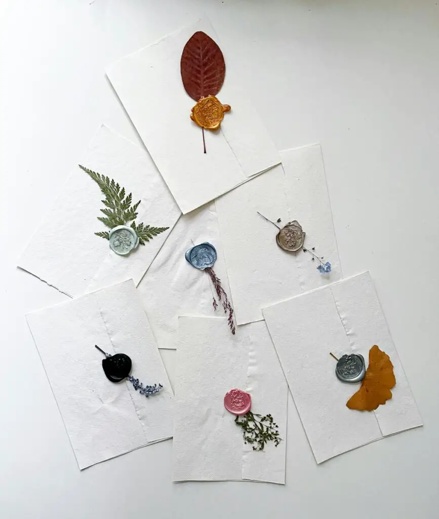 Flat lay of wax-sealed envelopes with pressed leaves offering artistic elegance on a white background.