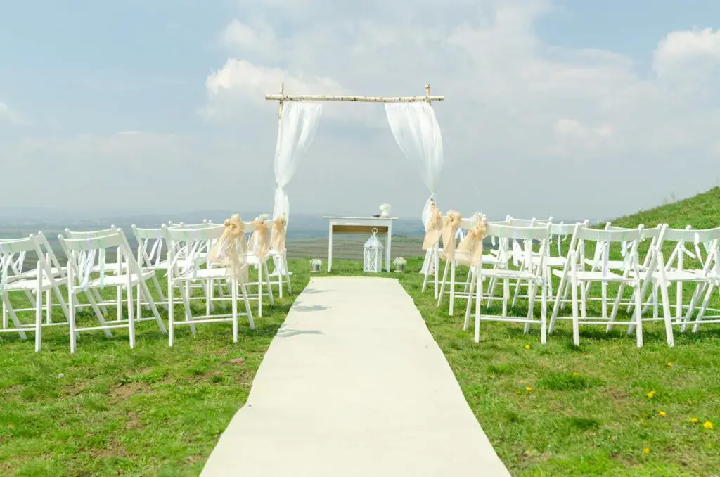 Elegant outdoor wedding setup with chairs and arch under a blue sky.